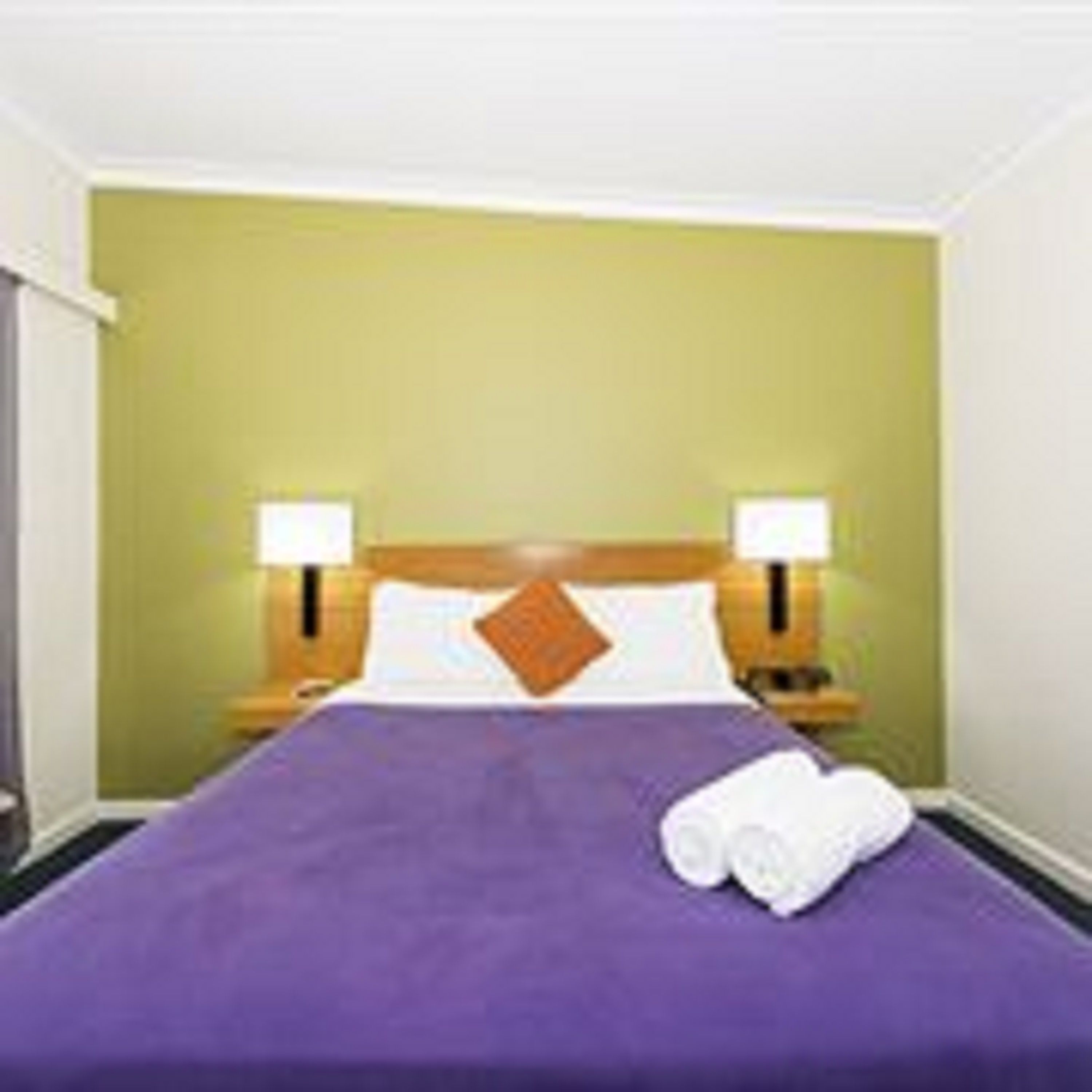 A hotel room with a bed, two bedside lamps, and a green wall.