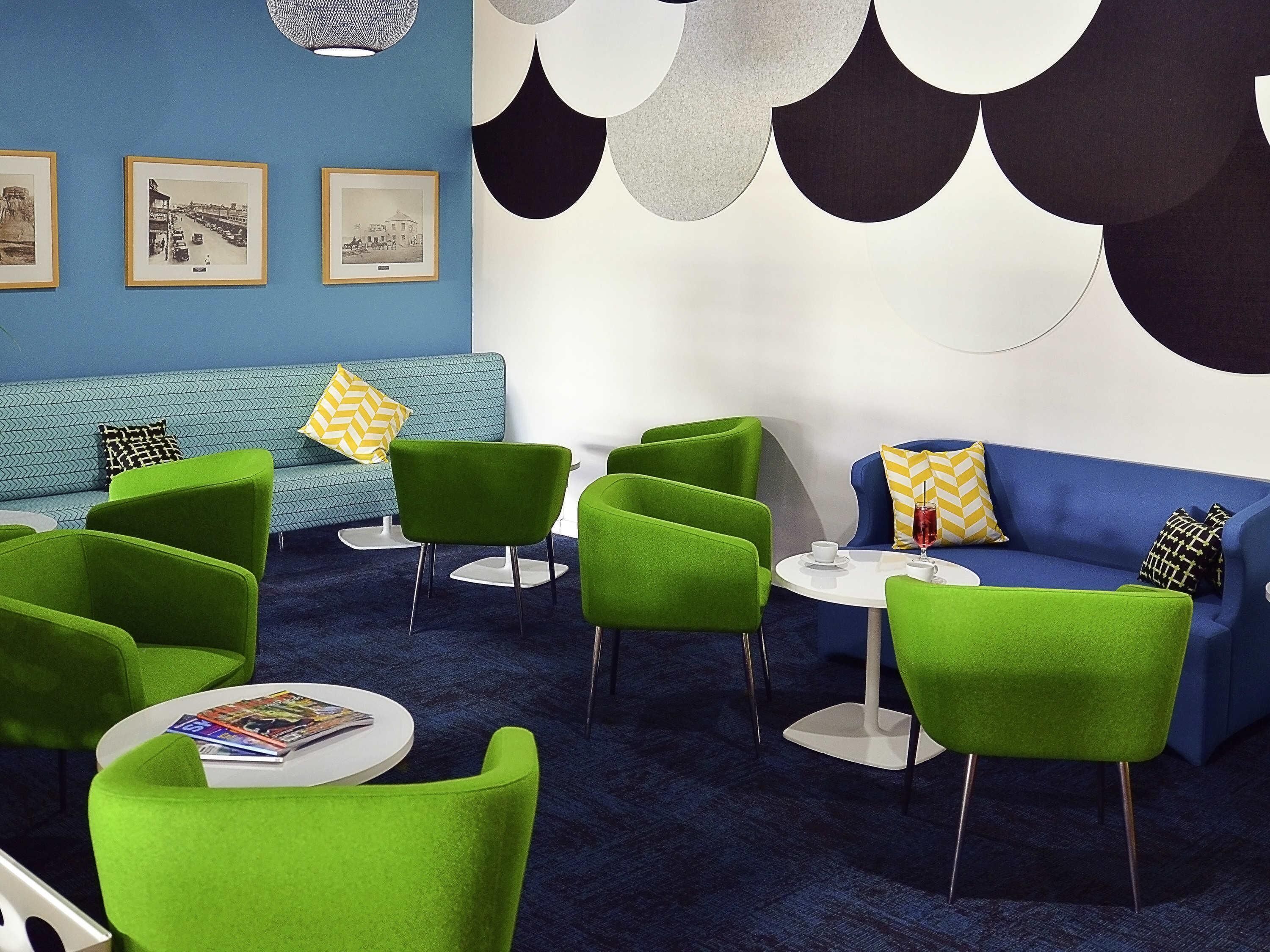 A modern lounge area with green chairs, a blue sofa, and a round table with a glass.
