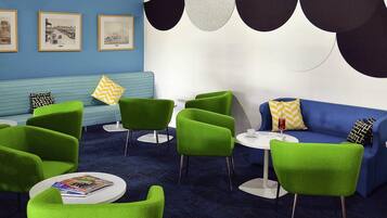 Uma área de estar moderna com cadeiras verdes, um sofá azul e uma mesa redonda com um copo.