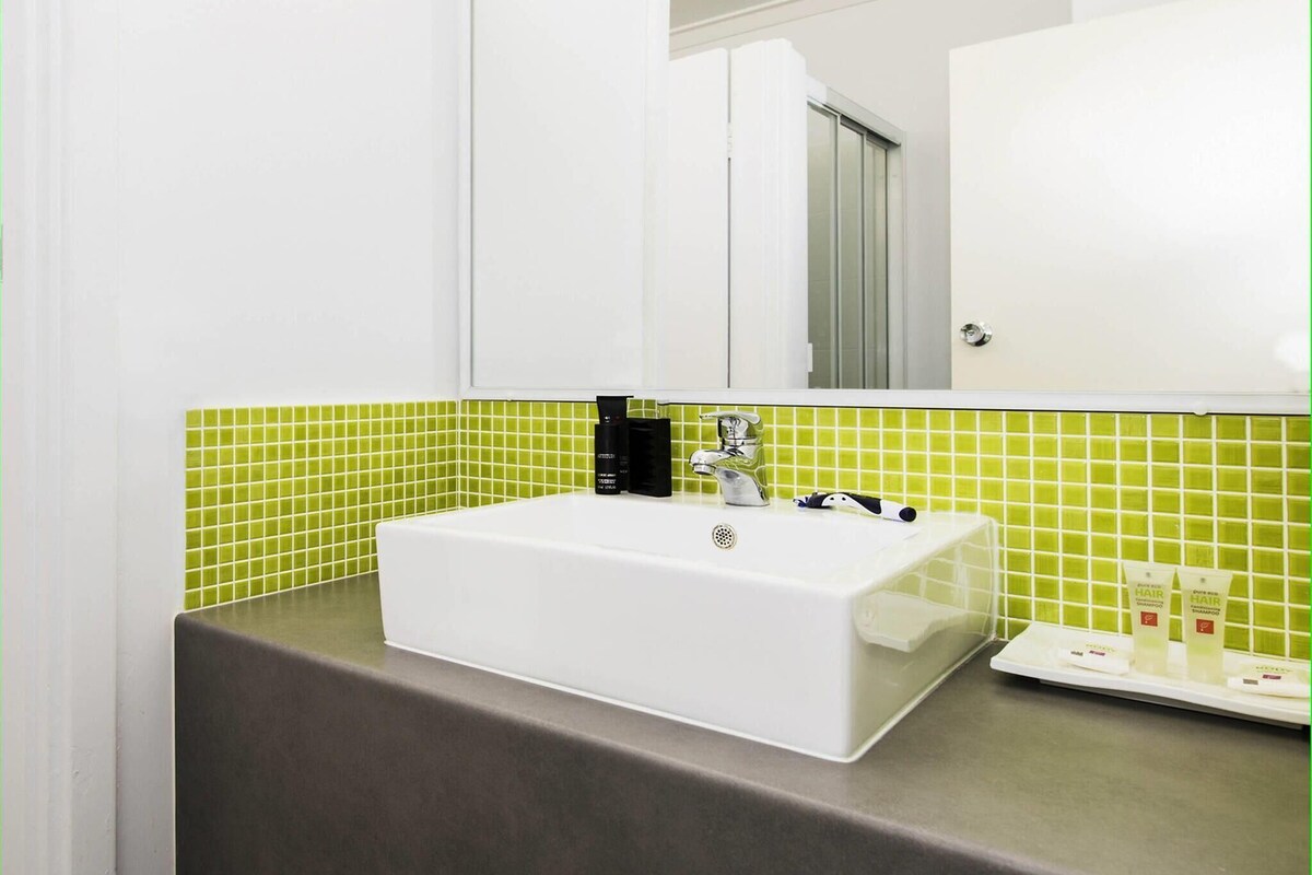 Un baño con lavamanos blanco, salpicadero de azulejos verdes y un espejo arriba.