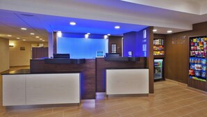 Un espace d’accueil d’hôtel comprenant un comptoir, un ordinateur et un réfrigérateur rempli de boissons.