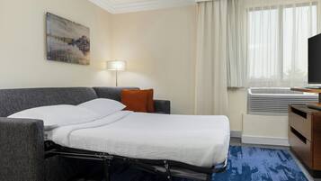 Et hotelværelse med sovemadras, fladskærms-TV, lampe og et billede på væggen.