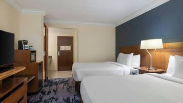Una habitación de hotel con dos camas, televisión, escritorio y lámpara.