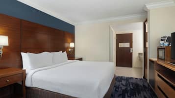 Quarto de hotel com uma cama grande, cabeceira de madeira, mesa de cabeceira, escrivaninha com um computador e uma televisão.