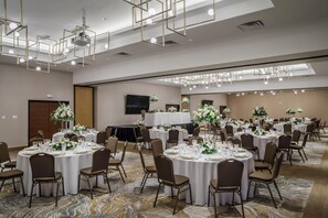 Un salón de banquetes con mesas redondas dispuestas para comer, equipado con sillas y cubiertos.