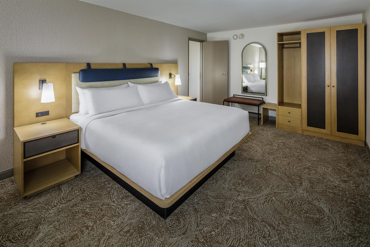 Habitación de hotel con una cama grande, una mesita de noche, un escritorio, un armario y un espejo.