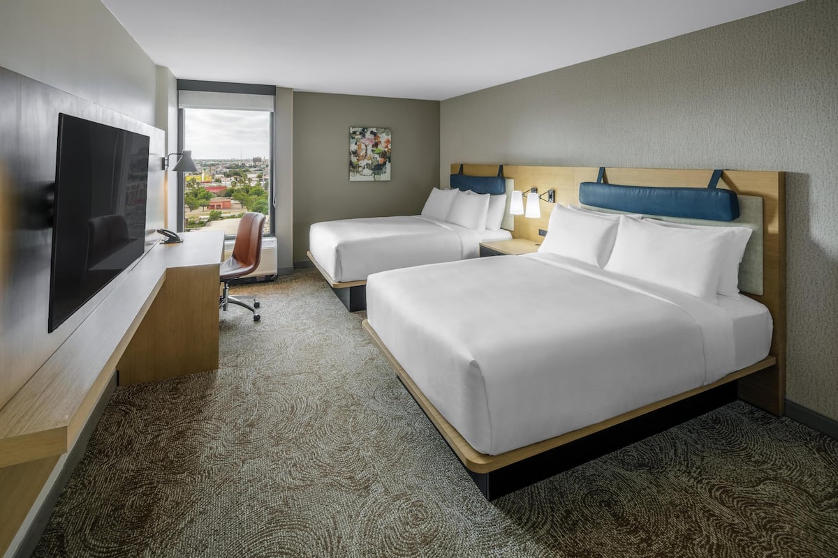 Habitación de hotel con dos camas, un escritorio, un televisor y vistas a la ciudad.