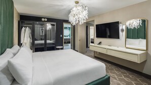A hotel room with a large bed, a vanity with a mirror, a chandelier, and a walk-in closet with robes. - DoubleTree by Hilton Laredo (Laredo)