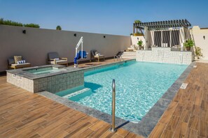 Une piscine sur le toit, dotée d’une terrasse en bois, d’un petit jacuzzi et d’une pergola ornée de plantes.