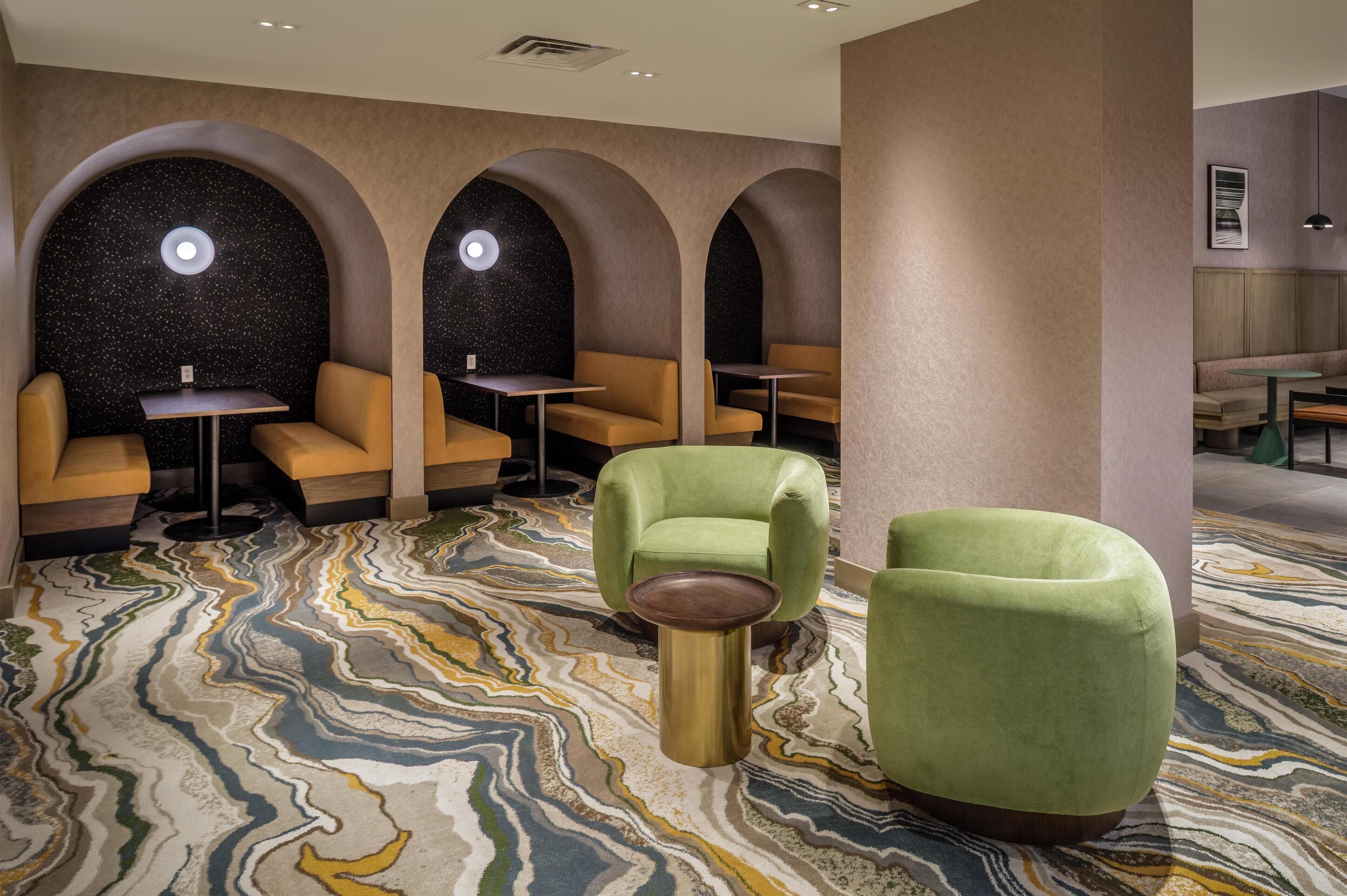 A modern lounge area with seating arrangements, including sofas and chairs, and a patterned carpet.