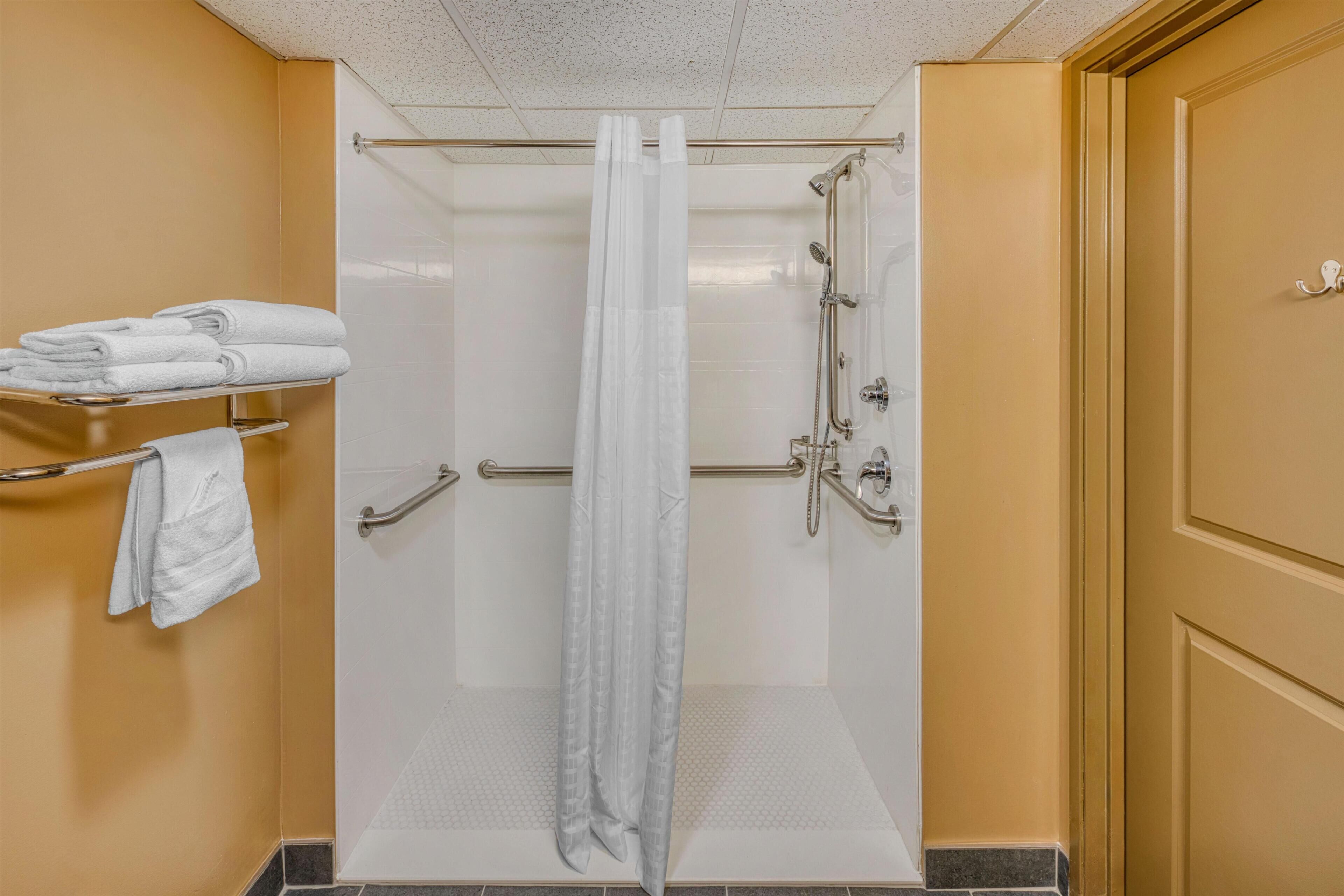 A shower with a glass door, a towel rack with folded towels, and a shower control panel.