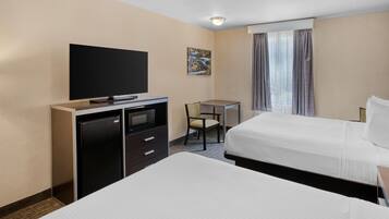 A hotel room with two beds, a desk, a television, and a small refrigerator.