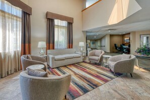 Un hall de hotel con un sofá, sillones, un tapete a rayas y un comedor con sillas.