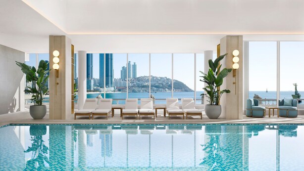 A modern indoor pool area with a clear view of the city skyline and sea. - The Westin Josun Busan (Busan)