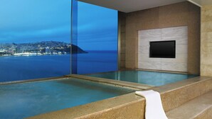 A modern indoor swimming pool with a city view, a flat-screen TV mounted on the wall, and a stone-textured floor. - The Westin Josun Busan (Busan)
