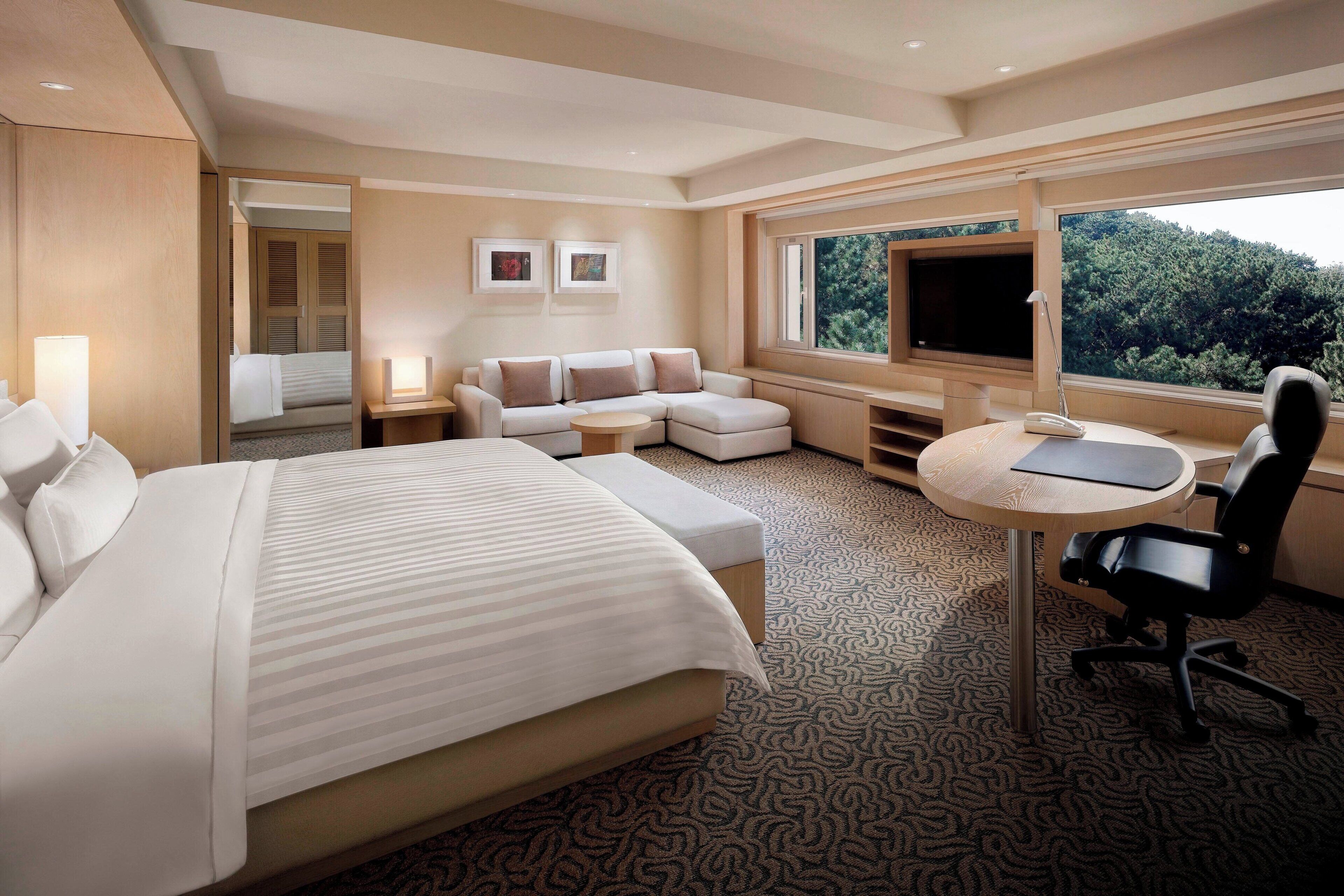 Una habitaci ón de hotel con una cama grande, un sofá, un escritorio con una silla, un televisor y una ventana con vista a árboles.