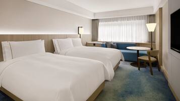 A hotel room with two beds, a small round table, a chair, and a TV.