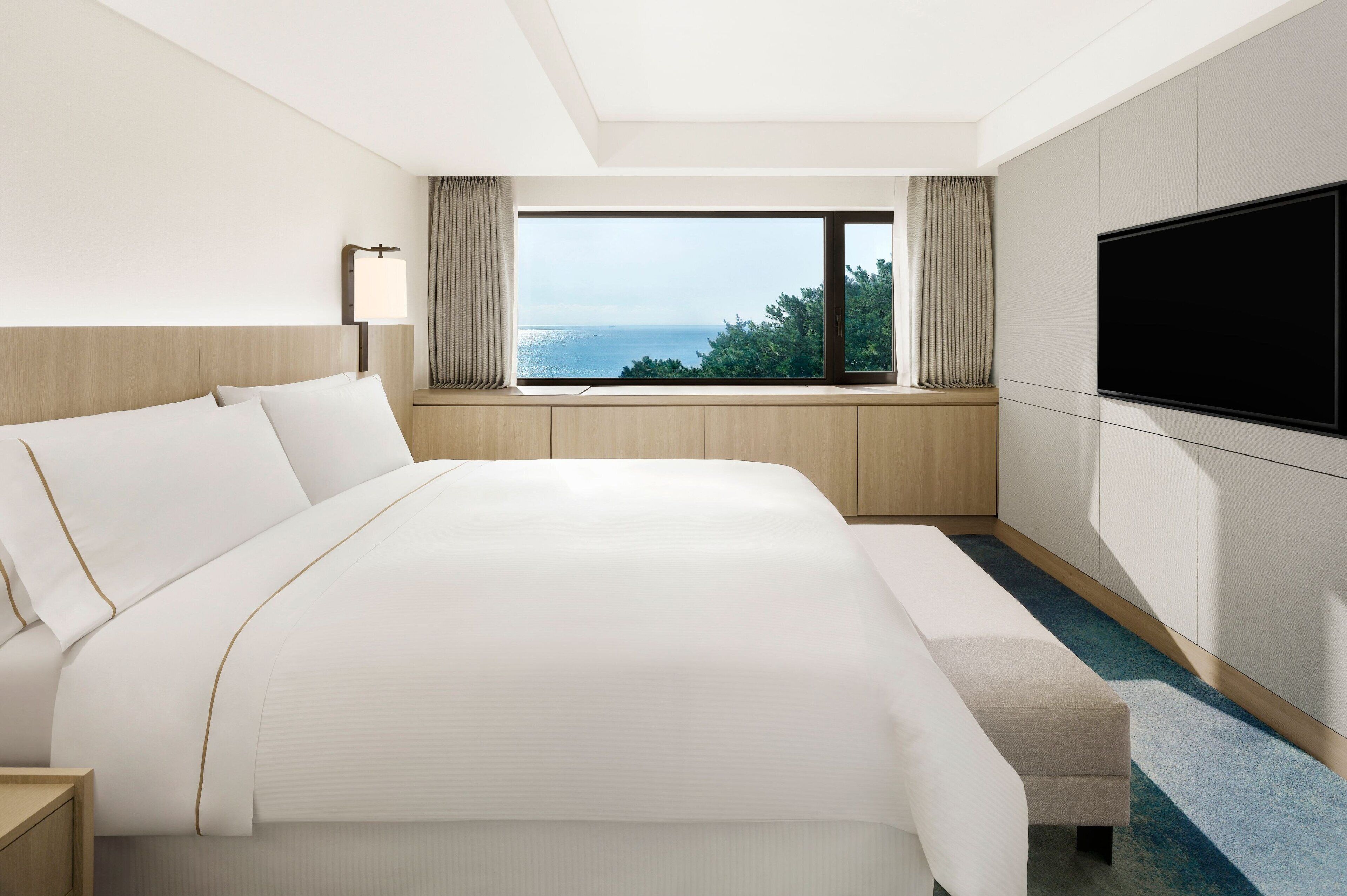 A hotel room with a large bed, a TV mounted on the wall, and a window with a view of the sea.