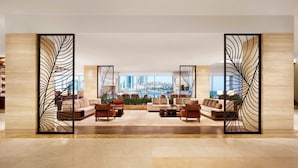 A spacious lobby with a modern design, featuring a seating area with sofas and armchairs, a decorative black partition, and a large window offering a city view. - The Westin Josun Busan (Busan)