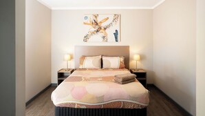 A neatly made bed with a patterned bedspread, two bedside lamps, and a wall-mounted abstract painting. - The Lodge Motel, Newman (Newman)