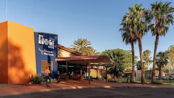 Motel Lodge con Seasons Steakhouse, con área de estar al aire libre cubierta y palmeras.