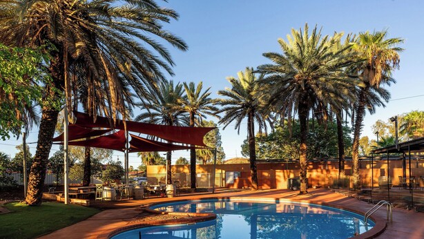 A swimming pool with a red canopy, surrounded by palm trees and a patio area with outdoor furniture. - The Lodge Motel, Newman (Newman)