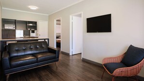 A modern living room with a black leather sofa, a wicker armchair, and a flat-screen TV mounted on the wall. - The Lodge Motel, Newman (Newman)