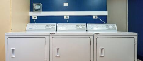 A laundry area with three stacked front-loading washers and dryers, a blue wall, and a white shelf above.