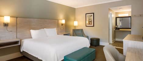A hotel room with a large bed, a bench, a chair, a desk, and a mirror.