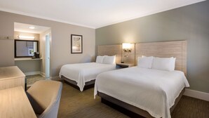 A hotel room with two beds, a desk, a chair, a nightstand, and a wall-mounted lamp.