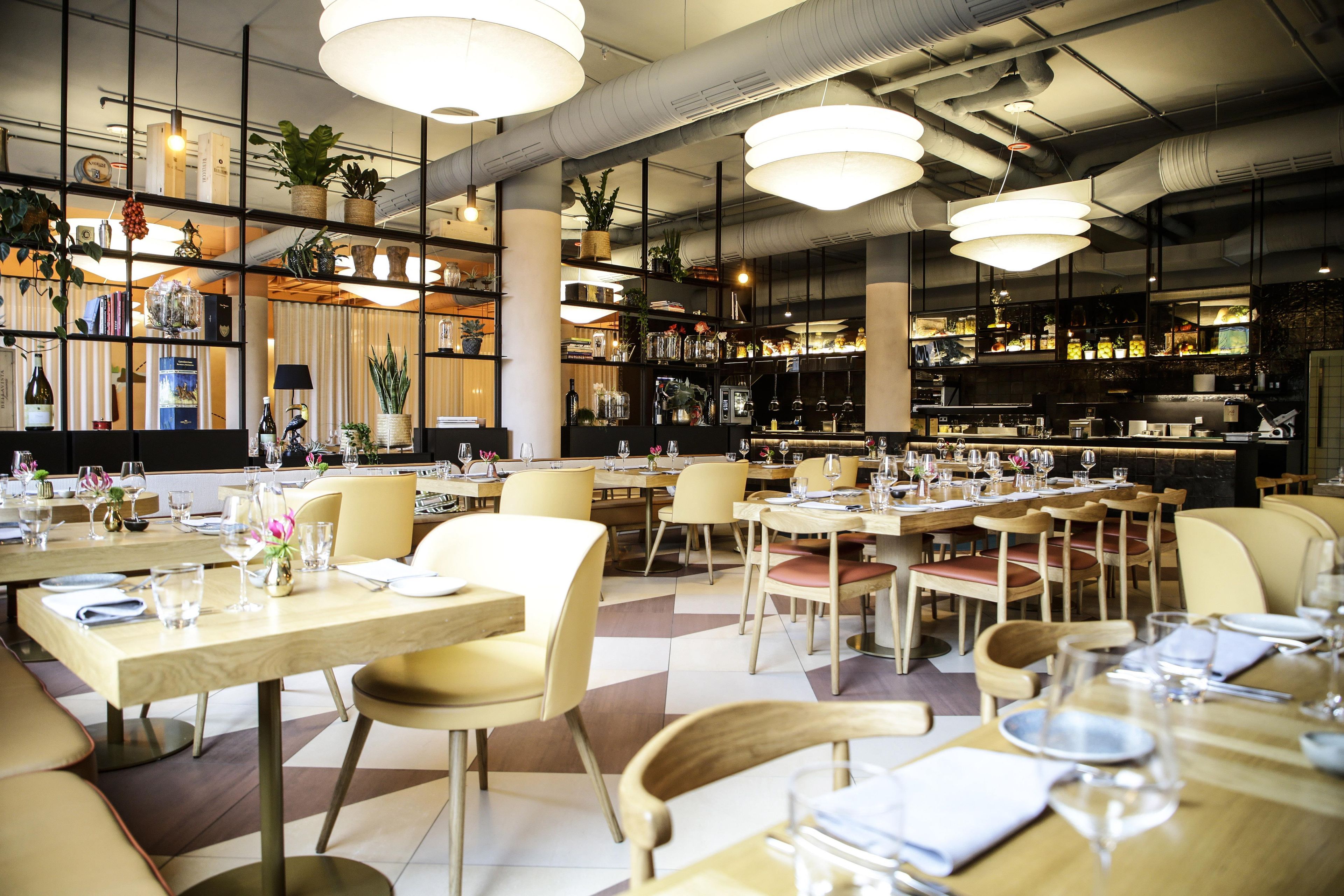 Interior de un restaurante con varias mesas, sillas y lámparas colgantes.