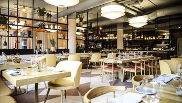Interior de un restaurante con varias mesas, sillas y lámparas colgantes.