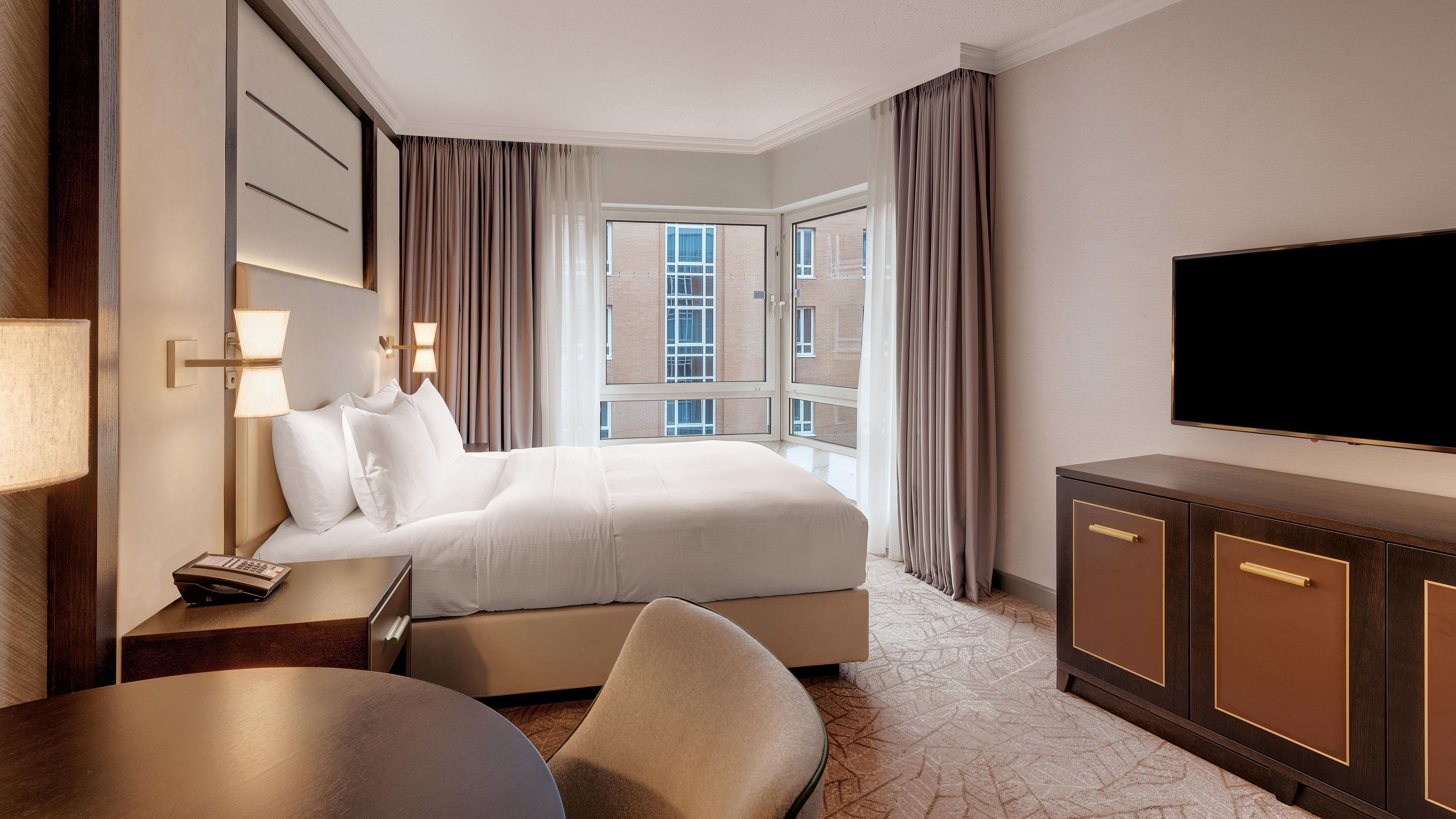 A hotel room with a bed, a desk, a chair, a television, and a window with curtains.