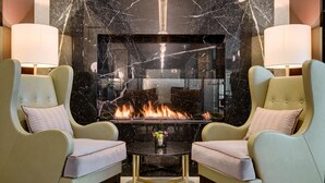 A modern lounge with two armchairs, a glass-top coffee table, and a fireplace with a visible fire. - Hilton Munich City (Munich)