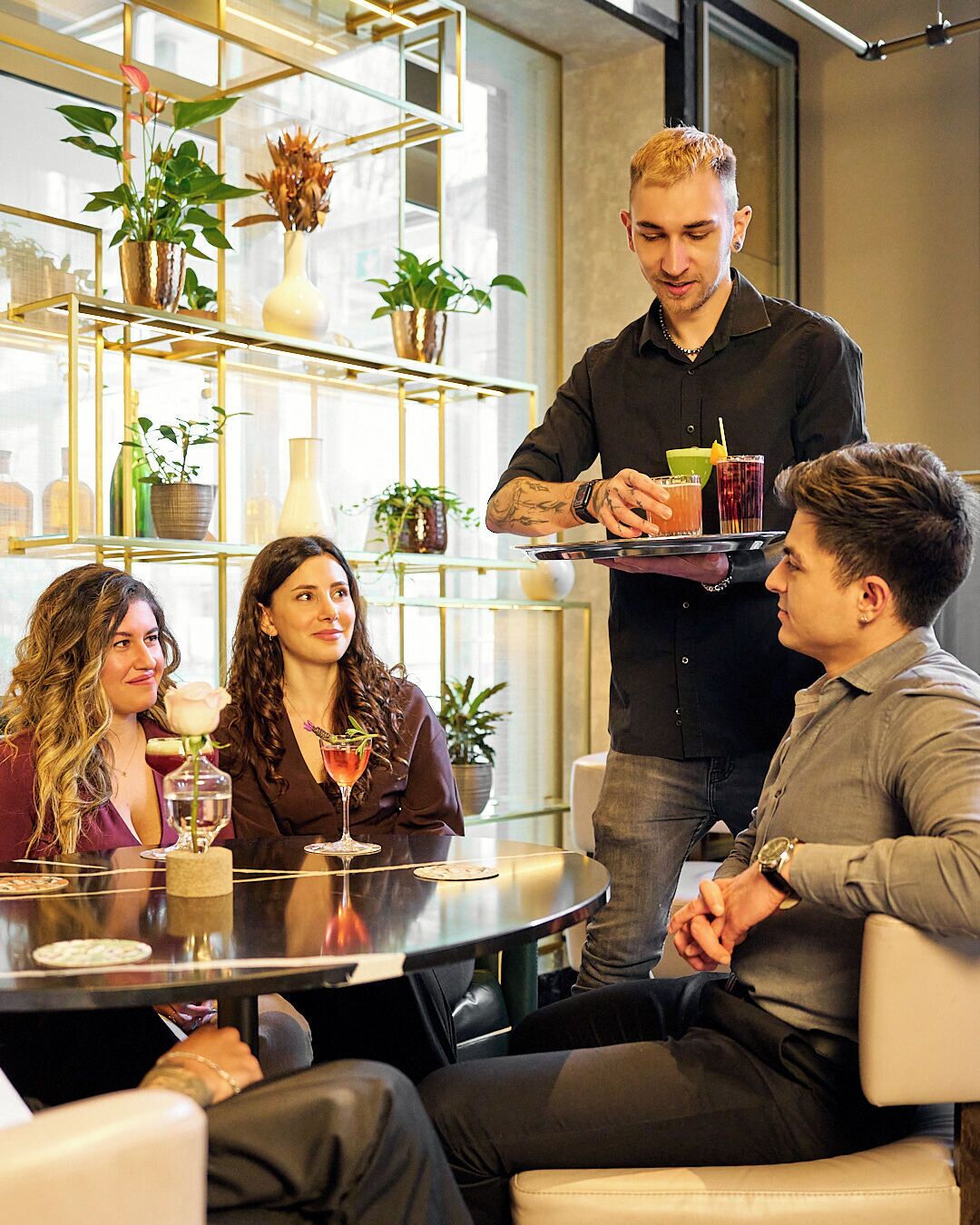 A modern interior with a round table, seating, and a waiter serving drinks.