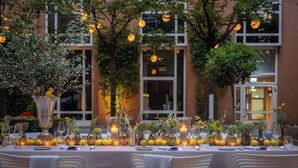 An outdoor dining area with a table set for a meal, surrounded by greenery and illuminated by string lights. - Hilton Munich City (Munich)