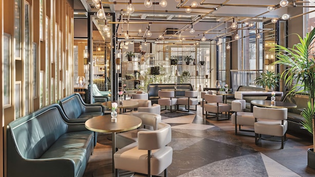 A modern interior with seating areas, tables, and a piano. - Hilton Munich City (Munich)