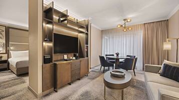 Una habitación de hotel moderna con cama, escritorio con televisor, zona de comedor con sillas y sofá.