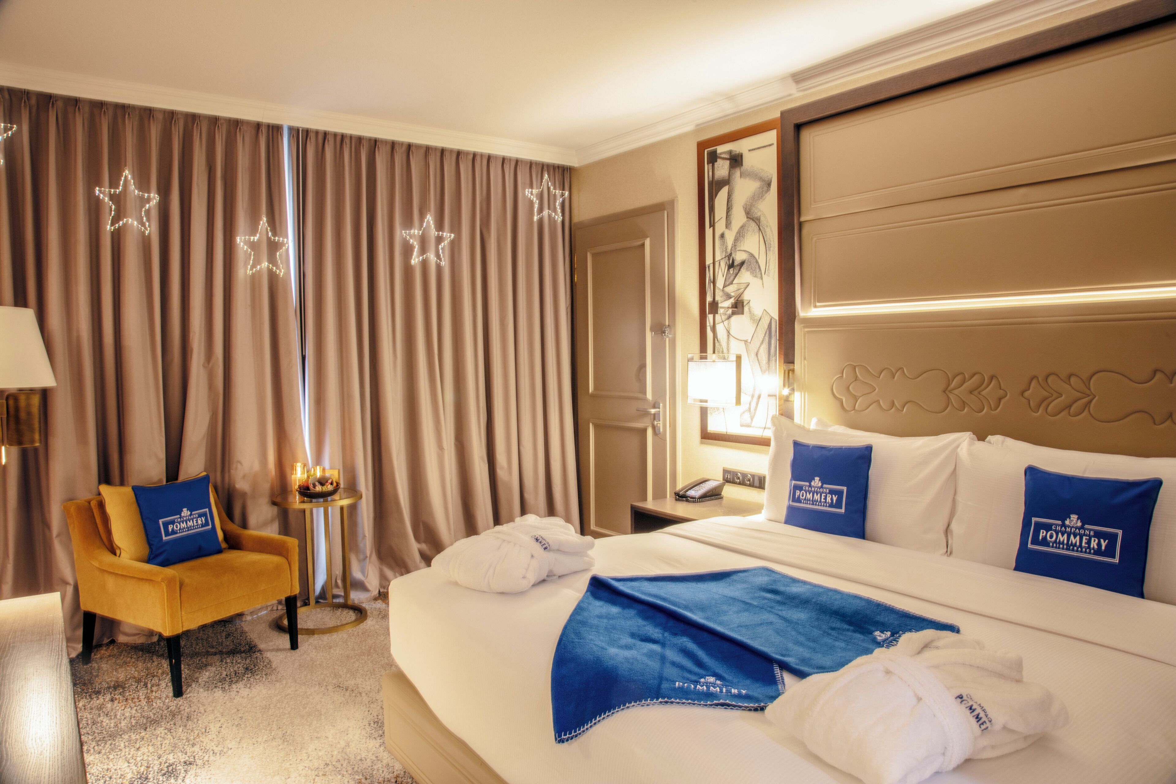 A hotel room with a large bed, a chair, a small table, and curtains with star decorations.