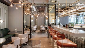 A modern bar area with a long counter, multiple stools, and a seating area with tables and chairs. - Hilton Munich City (Munich)