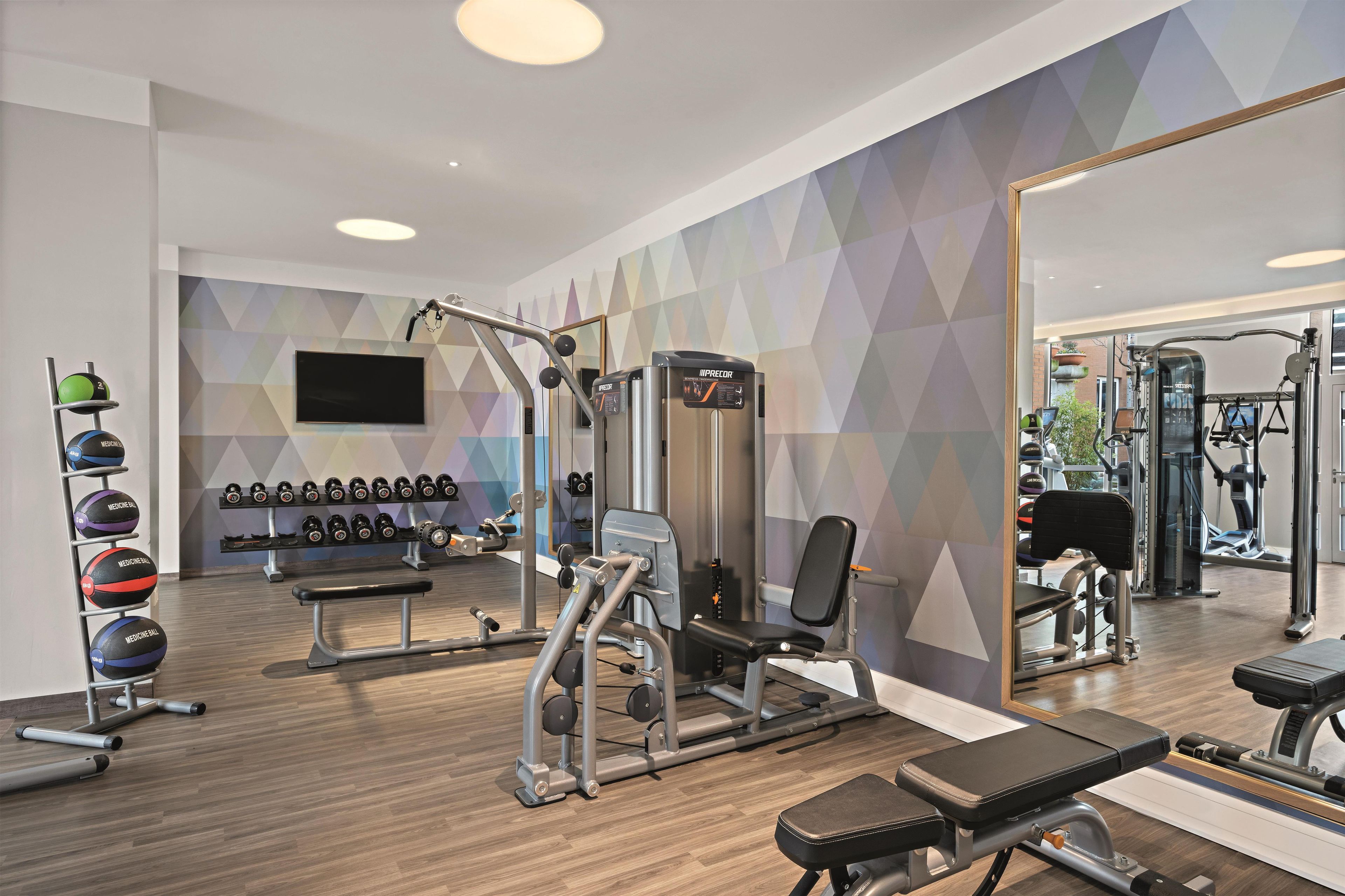 A gym with various exercise equipment, a bench, medicine balls, and a mirror.