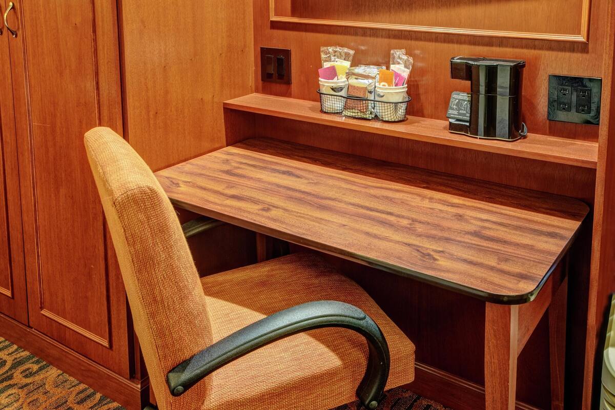 A wooden desk with a chair, a shelf with storage baskets, and electrical outlets.