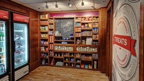 Interior de una tienda con estantes llenos de bocadillos y dulces, un letrero de pizarra que dice 'Sabor Local' y un cartel en la pared que dice 'Dulces'.