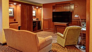 Habitación de hotel con sofá, sillón, televisión, kitchenette y alfombra estampada.