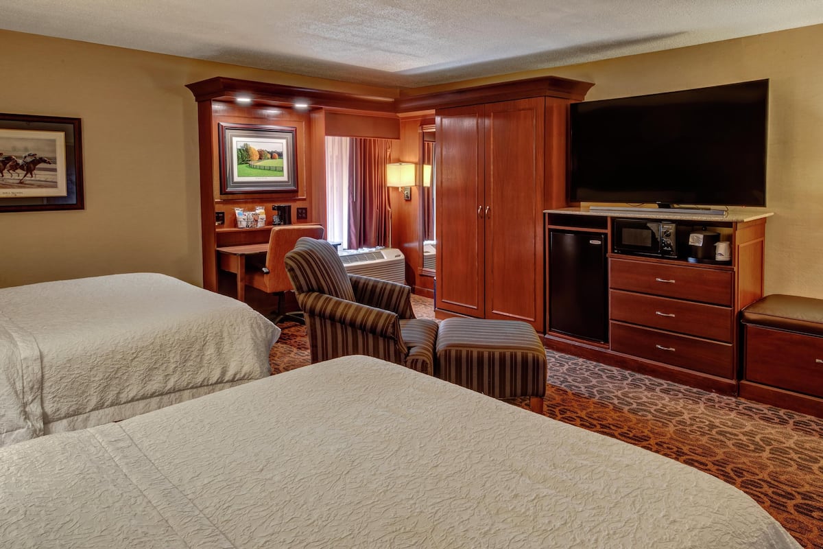 A hotel room with two beds, a desk with a chair, a television, a microwave, and a cabinet.