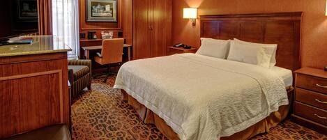 A hotel room with a bed, desk, chair, and a television.