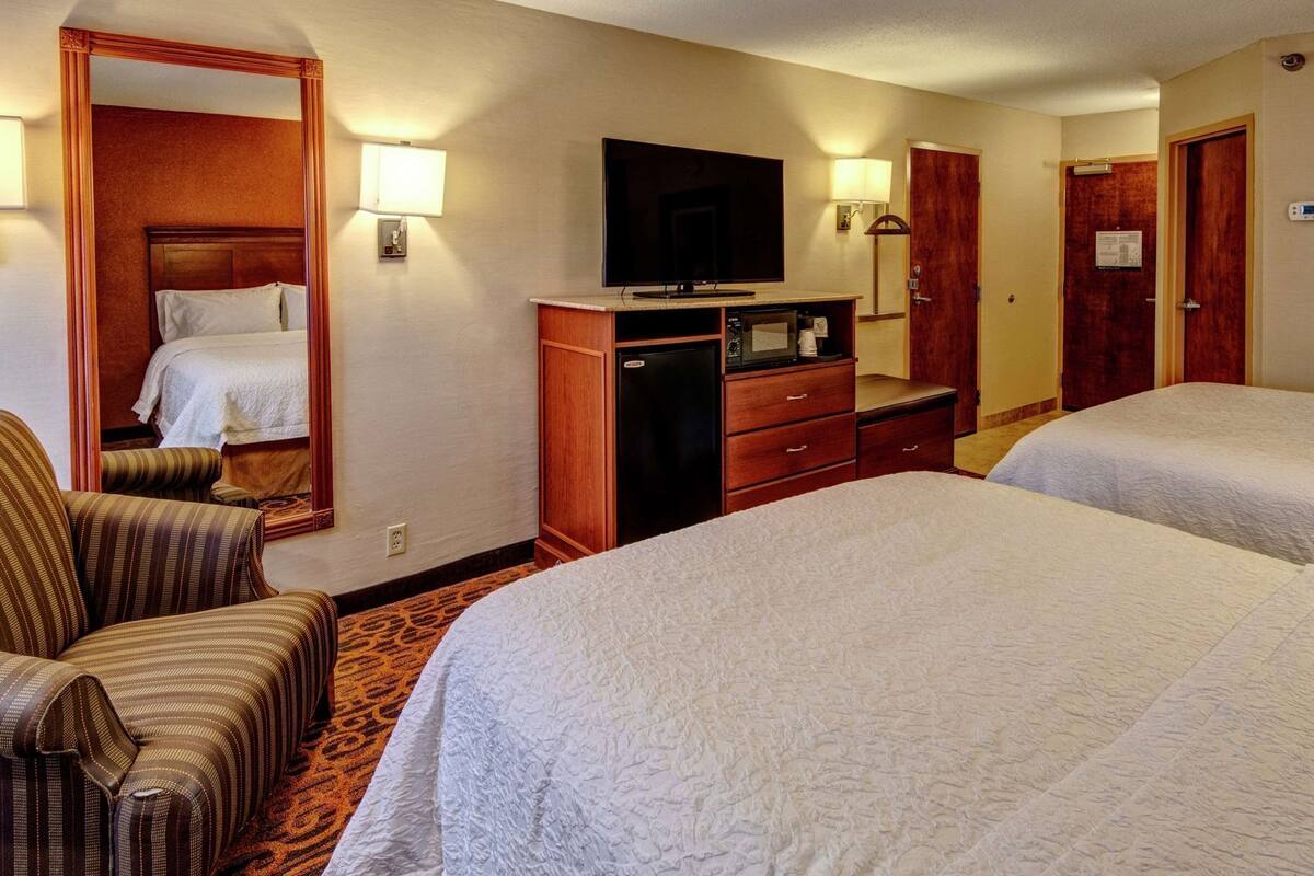 A hotel room with two beds, a television, a dresser, a chair, and a mirror.