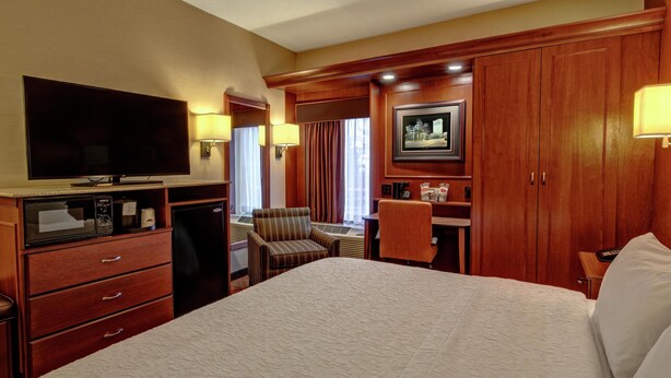 Habitación de hotel con una cama grande, televisión, escritorio con silla, armario y ventana con cortinas.