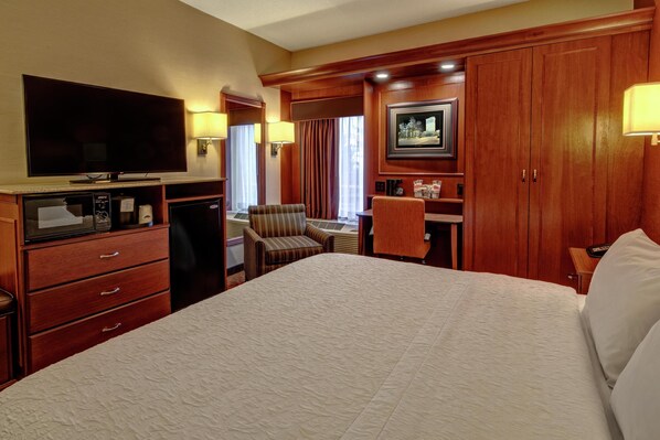Habitación de hotel con una cama grande, televisión, escritorio con silla, armario y ventana con cortinas.