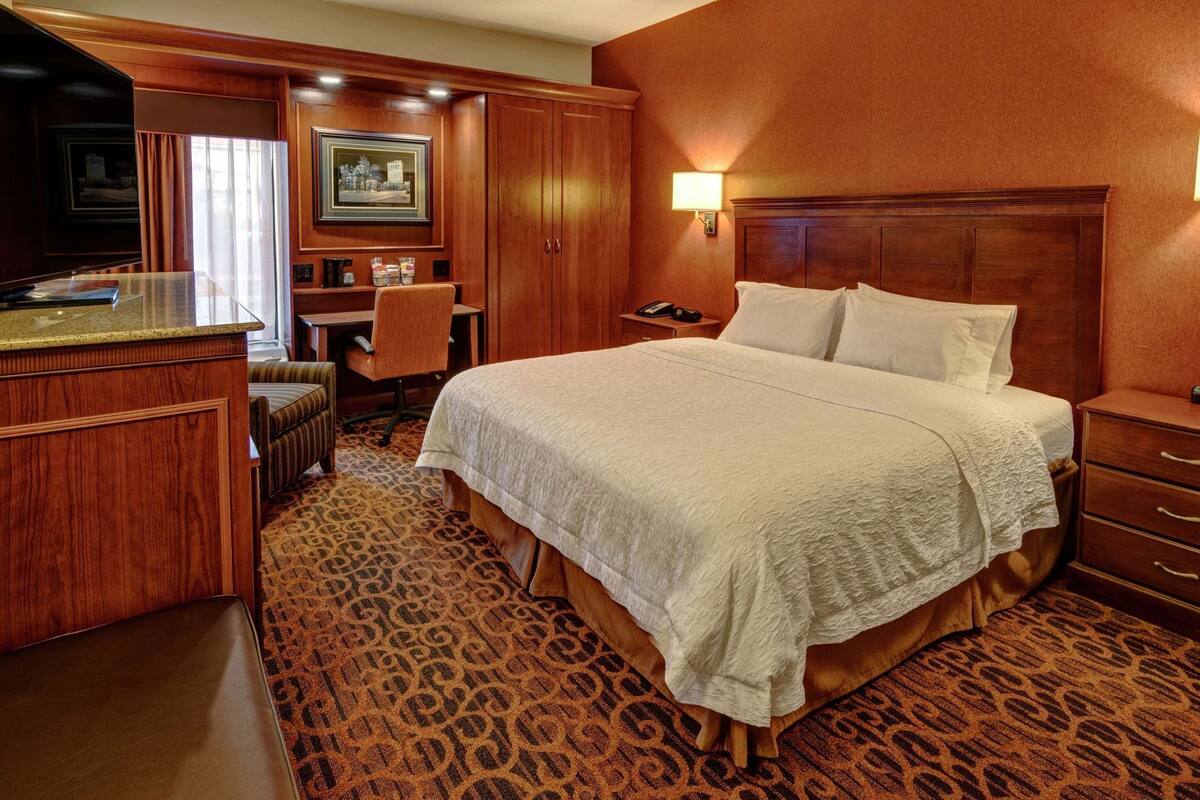 A hotel room with a large bed, a desk with a chair, a telephone, and a television.